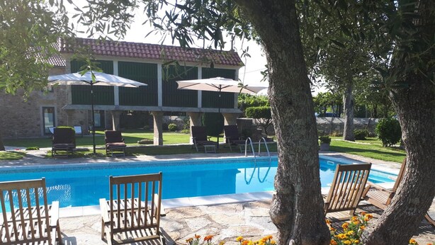 A pool area with lounge chairs and umbrellas, surrounded by a stone patio and a building with a tiled roof. - Torres de Moreda (A Estrada)