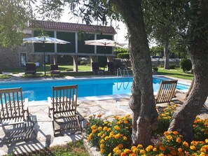 A pool area with lounge chairs and umbrellas, surrounded by a stone patio and a building with a tiled roof. - Torres de Moreda (A Estrada)