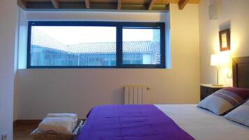 A bedroom with a large window, a bed with a purple bedspread, a bedside lamp, and a radiator.