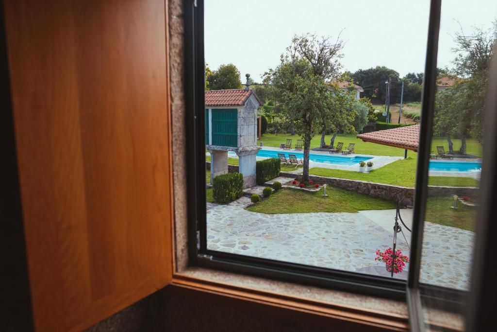 A view through a window of a swimming pool, a small building with a green door, and a stone pathway.