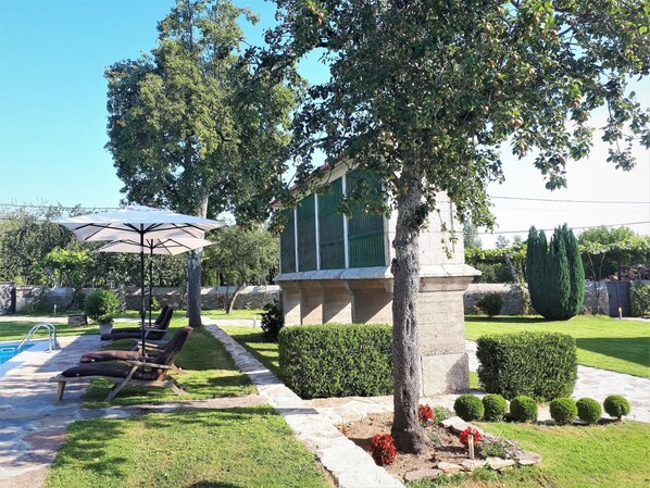 Un jardín bien cuidado con piscina, sillas de descanso y una estructura de piedra.