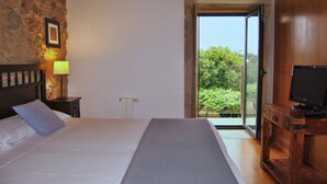 A bedroom with a bed, a nightstand, a TV stand, and a view of greenery through a glass door. - Torres de Moreda (A Estrada)