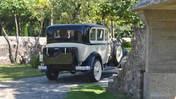 A vintage car parked on a cobblestone path beside a stone wall.