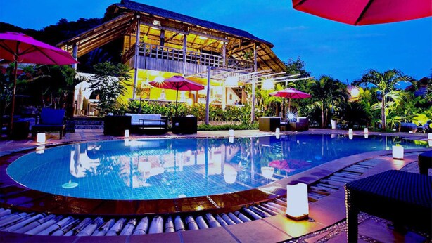 A pool area with lounge chairs and umbrellas, a building with a thatched roof, and a well-maintained garden. - Raingsey Bungalow (Kep)