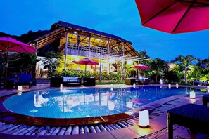 A pool area with lounge chairs and umbrellas, a building with a thatched roof, and a well-maintained garden. - Raingsey Bungalow (Kep)