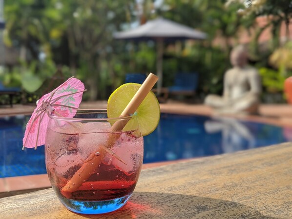 A glass of red drink with a lime slice and straw, placed on a wooden table by a pool. - Raingsey Bungalow (Kep)