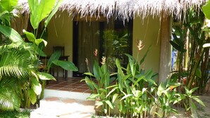 A thatched-roof structure with a tiled entrance, surrounded by lush tropical plants. - Raingsey Bungalow (Kep)