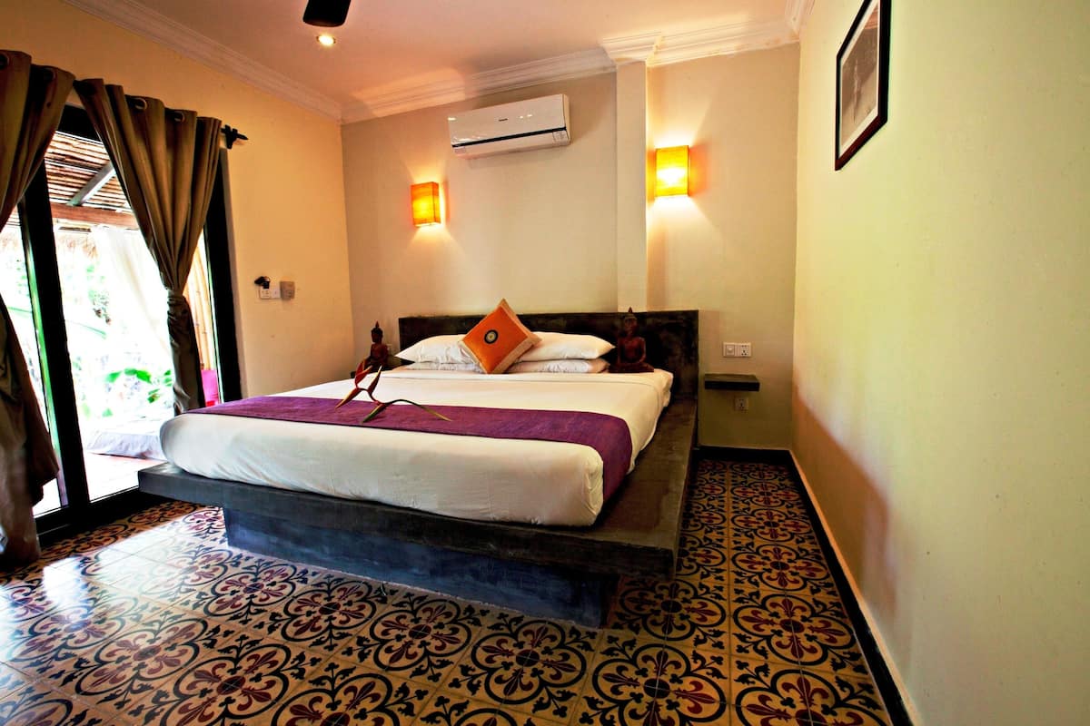 A hotel room with a bed, an air conditioner, and two wall-mounted lights.