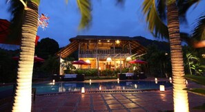 Un resort con piscina, palmeras y un edificio de techo de paja.