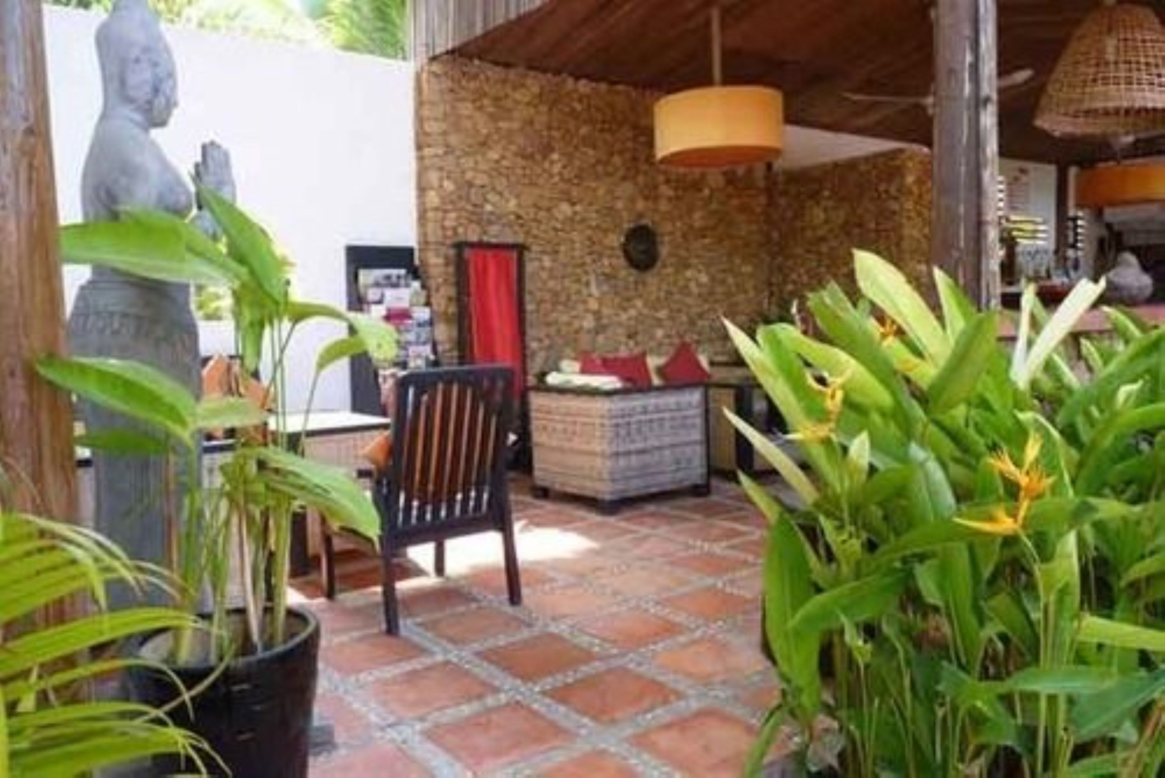 A patio area with a stone wall, a statue, a chair, and potted plants.