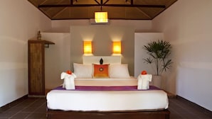 A hotel room with a bed, two bedside lamps, a nightstand, a potted plant, and a wooden cabinet. - Raingsey Bungalow (Kep)