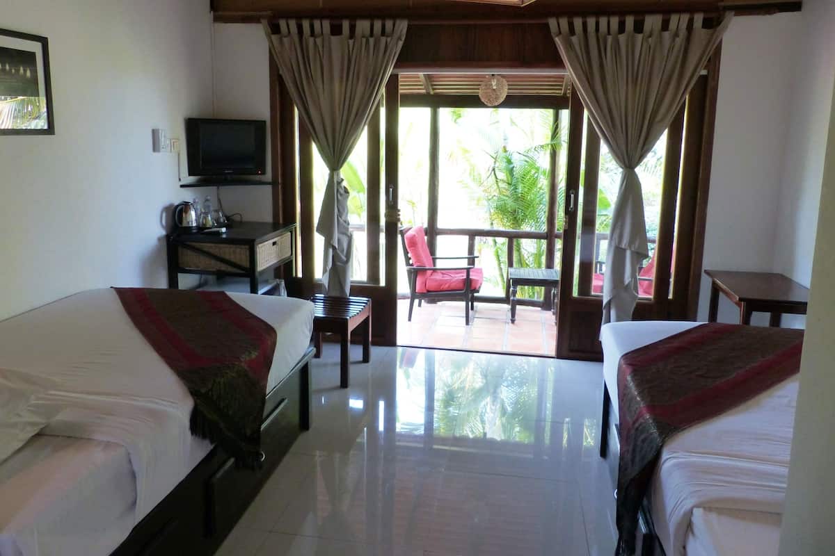 A hotel room with two beds, a TV, a desk, and a balcony with a chair and table.