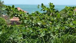 A lush green landscape with a view of the ocean and a building with a red roof in the background. - Raingsey Bungalow (Kep)