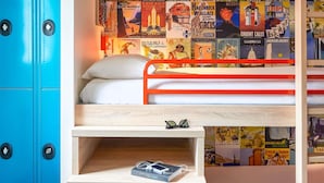 Un lit superposé avec une plateforme en bois et une étagère, une armoire bleue et un mur décoré d’anciennes affiches de voyage.