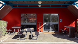 L’entrée d’un hôtel, avec une façade rouge, une enseigne jaune indiquant « hotelFL.com », et un espace extérieur aménagé avec des tables et des bancs.