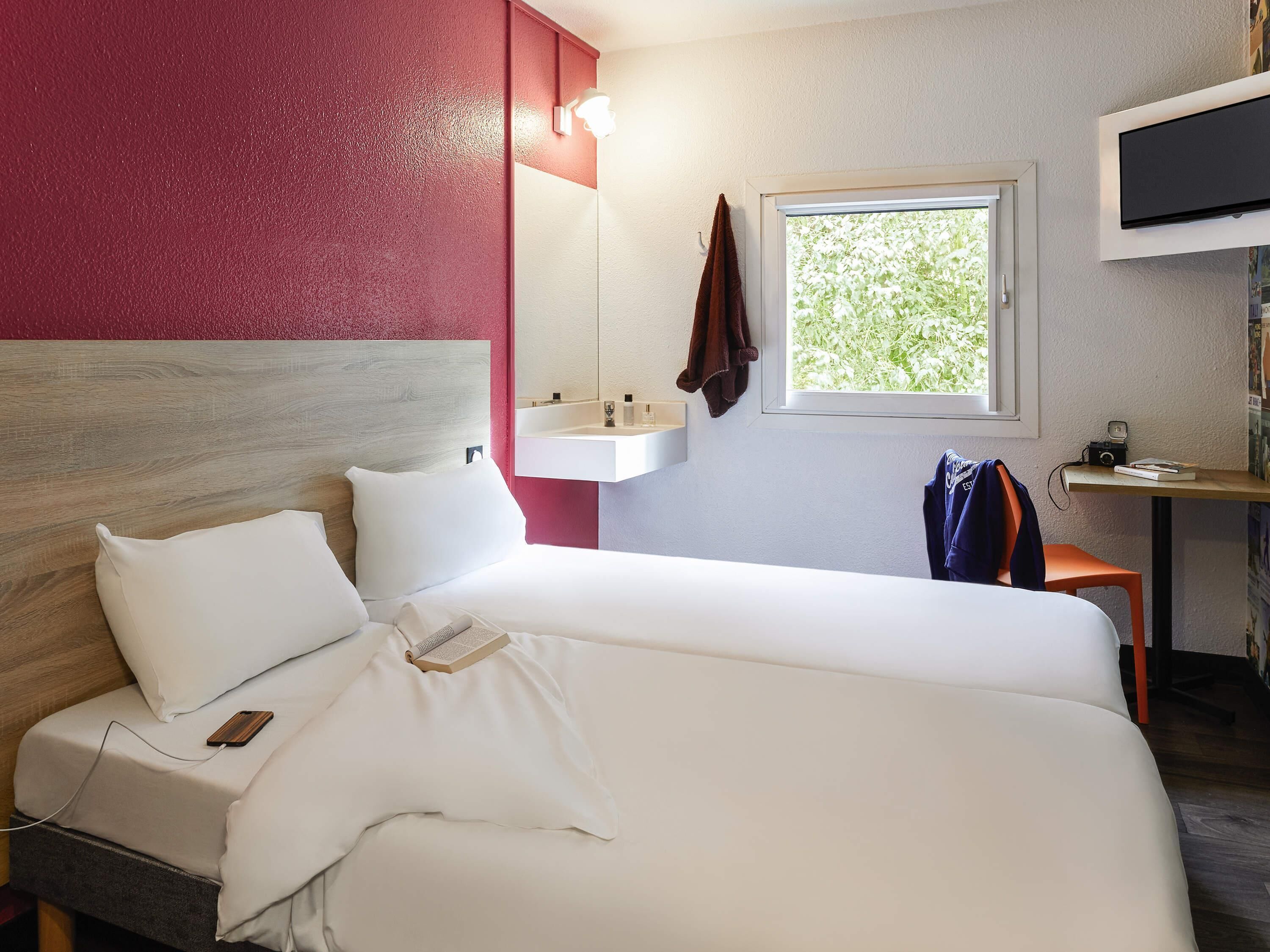 A hotel room with a bed, a bedside table, a TV, a window, and a sink.
