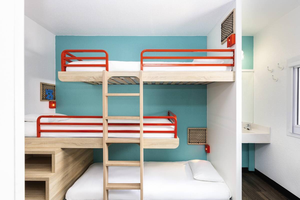 A bunk bed room with a wooden ladder, a white sink, and a window.