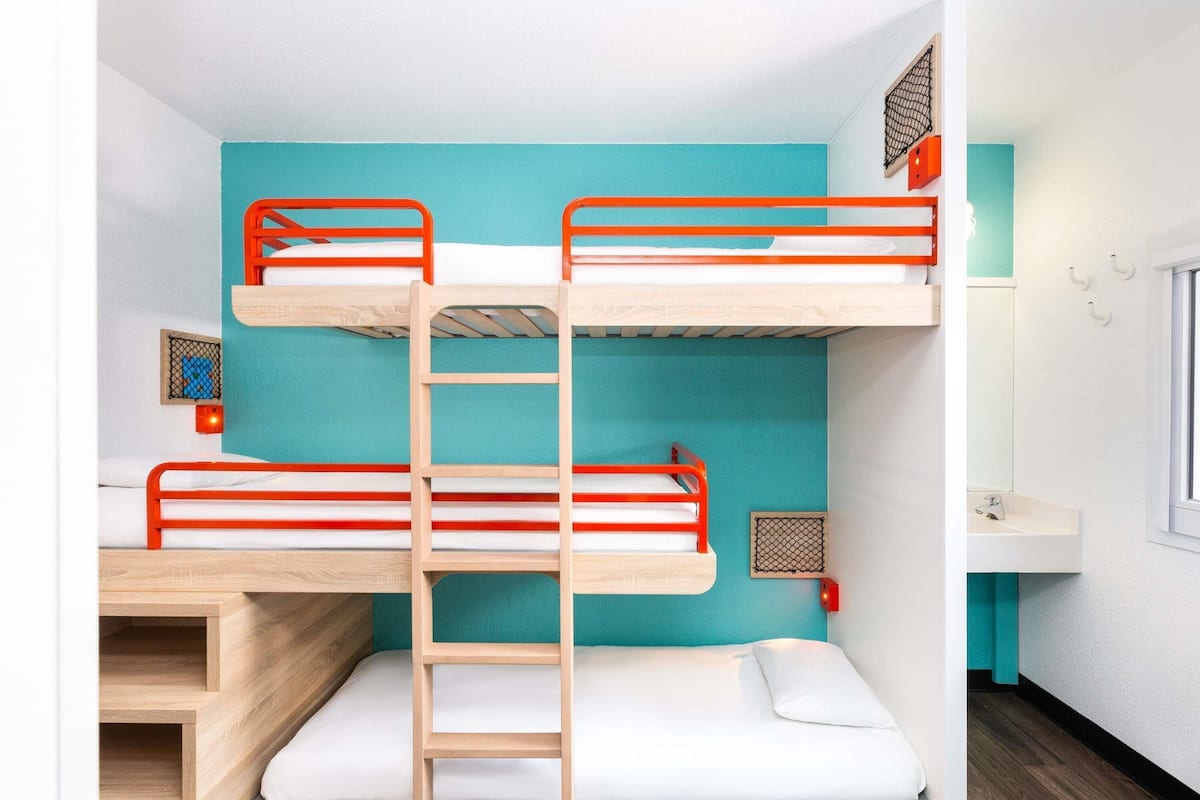 Dormitorio con literas, una escalera de madera, un lavabo blanco y una ventana.