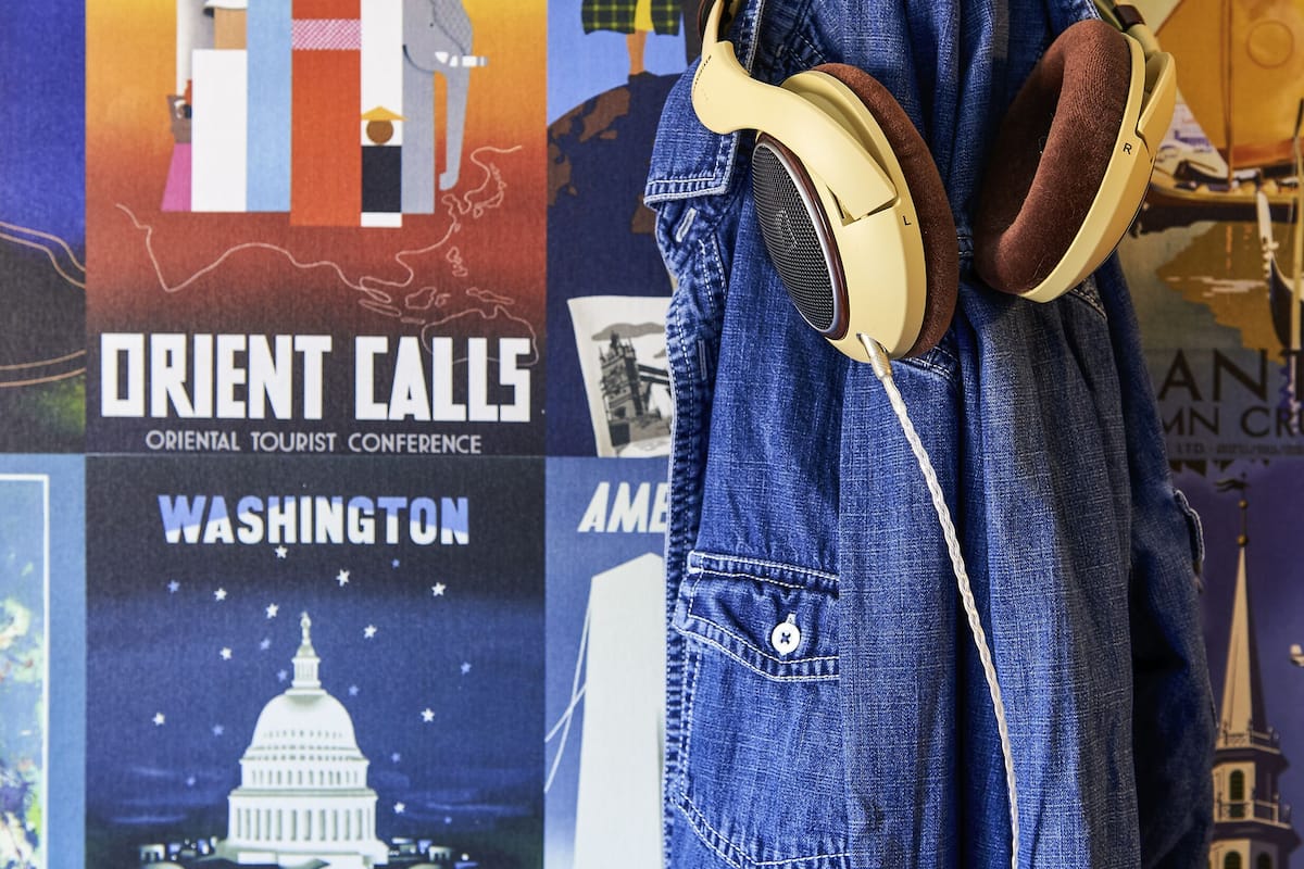 A denim jacket with headphones hanging on a wall adorned with various travel posters.