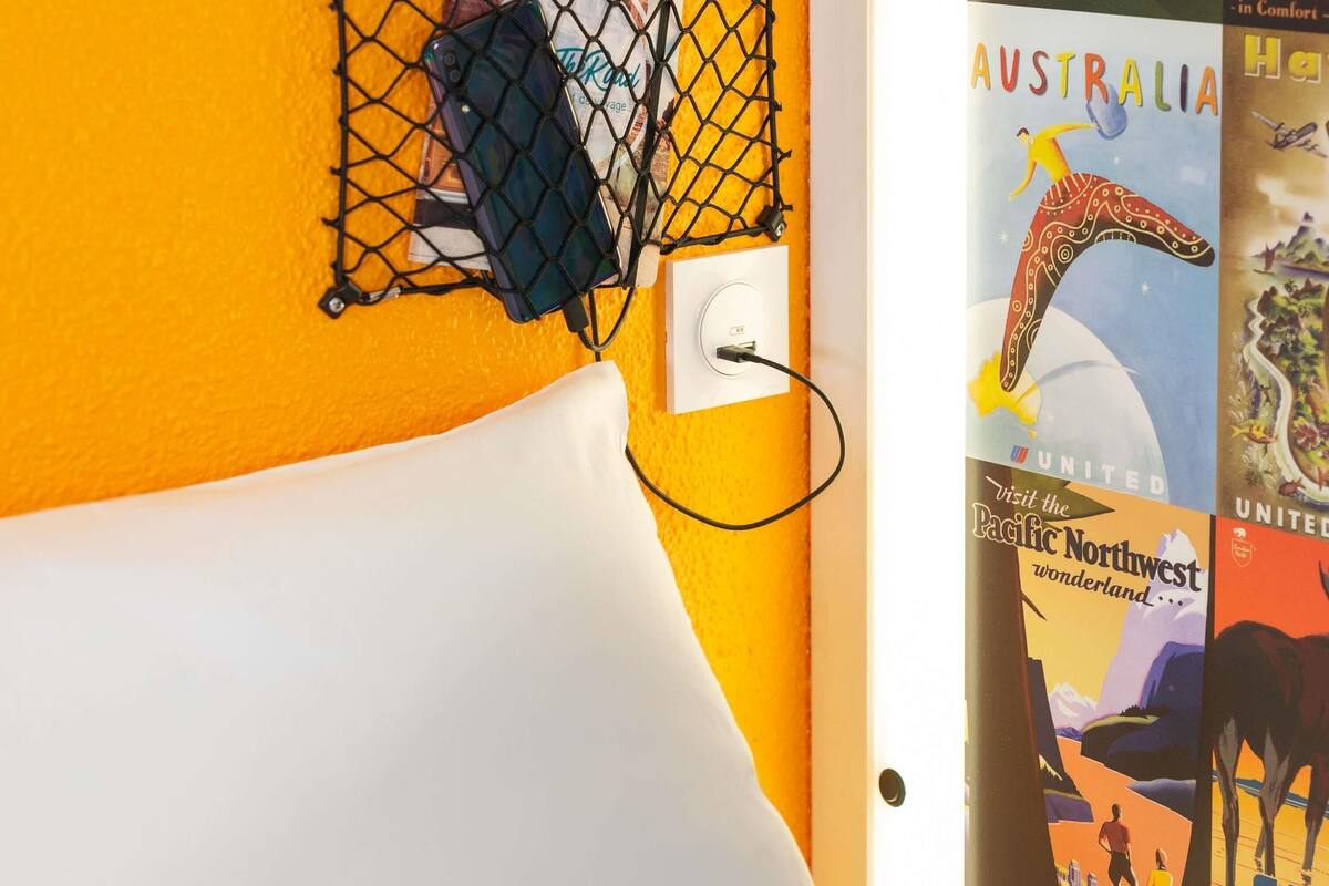 A room with a white bed, a black phone on a charging stand, and travel posters on the wall.