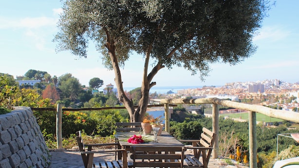 A stone patio with wooden benches and a table, overlooking a cityscape. - Camping Tropical (Almunecar)