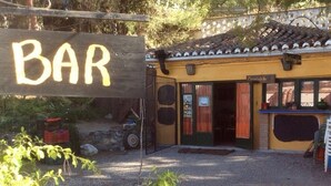 A rustic bar with a wooden sign, a tiled roof, and outdoor seating. - Camping Tropical (Almunecar)