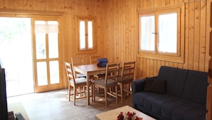 A wooden cabin with a dining area, a sofa, and large windows. - Camping Tropical (Almunecar)
