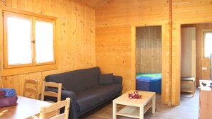 A wooden cabin interior with a sofa, a small table, and a bed. - Camping Tropical (Almunecar)