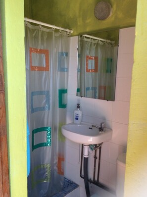 A bathroom with a shower curtain featuring geometric patterns, a white sink with a soap dispenser, and a mirror above the sink. - Camping Tropical (Almunecar)