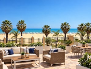 A terrace with outdoor furniture, a view of the beach, and palm trees. - Hotel Riviera Palace (Porto Empedocle)