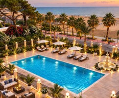 Una piscina con lettini e ombrelloni, circondata da palme e vista sulla spiaggia.