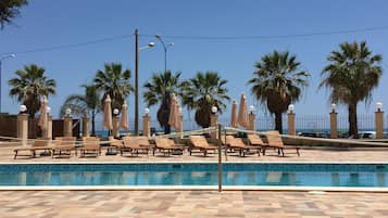 Una piscina al aire libre, sombrillas, sillones reclinables de piscina