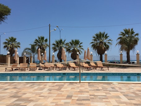 Una piscina al aire libre, sombrillas, sillones reclinables de piscina