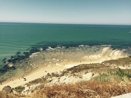 Paesaggio costiero con spiaggia, acqua cristallina e vegetazione rada.