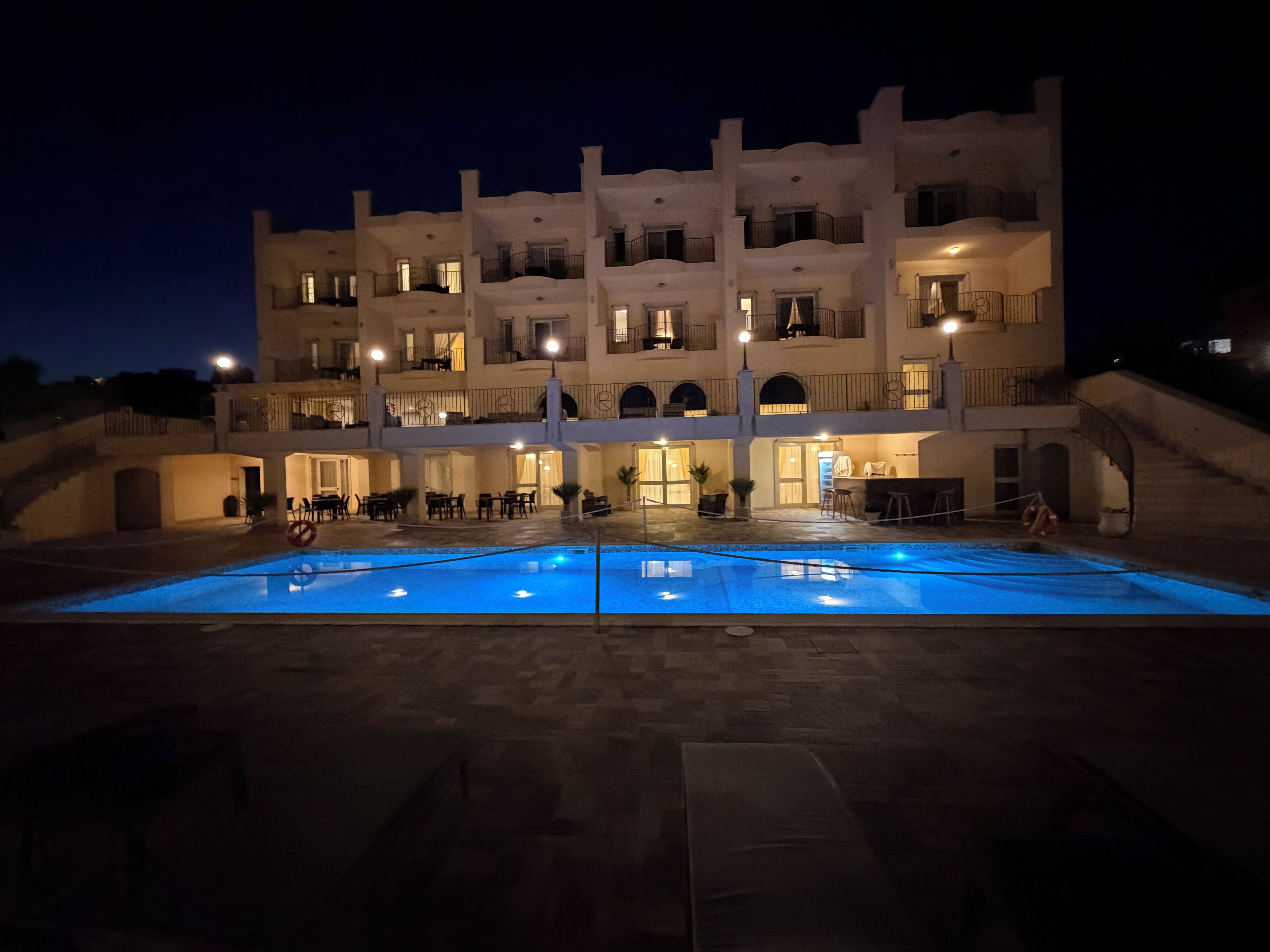 A multi-story hotel with a swimming pool, outdoor seating, and a staircase leading to the upper floors.