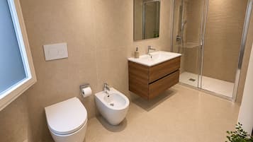 Un baño moderno con inodoro, bidé, tocador, espejo y cabina de ducha de vidrio.