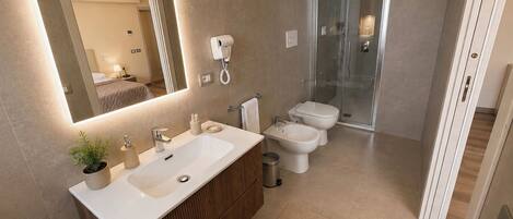 A modern bathroom with a large mirror, dual sinks, a toilet, and a glass shower enclosure.