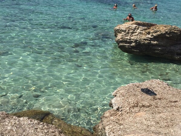 A clear, shallow water body with visible rocks and a few people swimming. - Hotel Riviera Palace (Porto Empedocle)