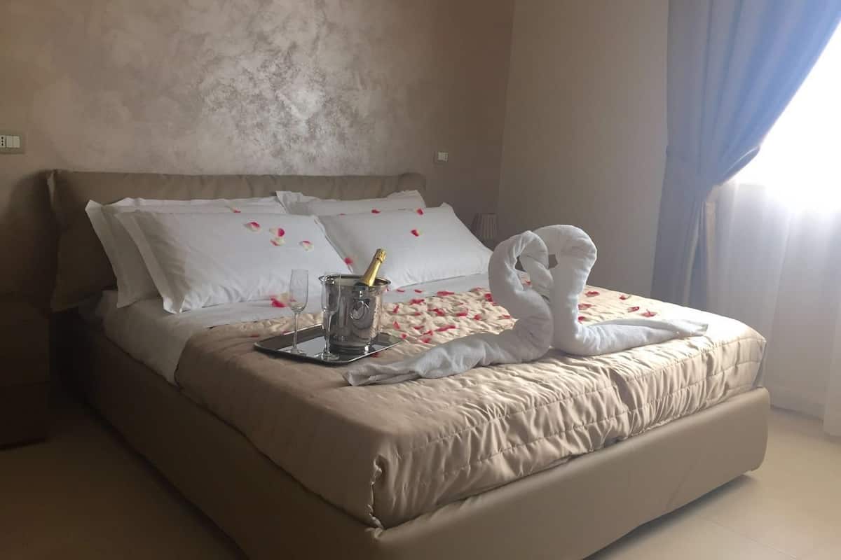 A hotel room with a bed, a bedside table with a champagne bottle and glass, and a decorative swan towel on the bed.