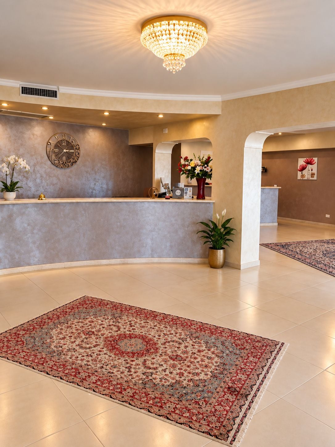 Rebuda d'hotel amb taulell de recepció, una gran pèndol, un rellotge i una catifa amb motius.