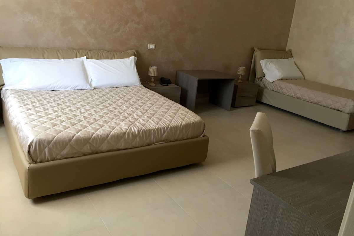 A bedroom with a large bed, a small desk, a chair, and a sofa.