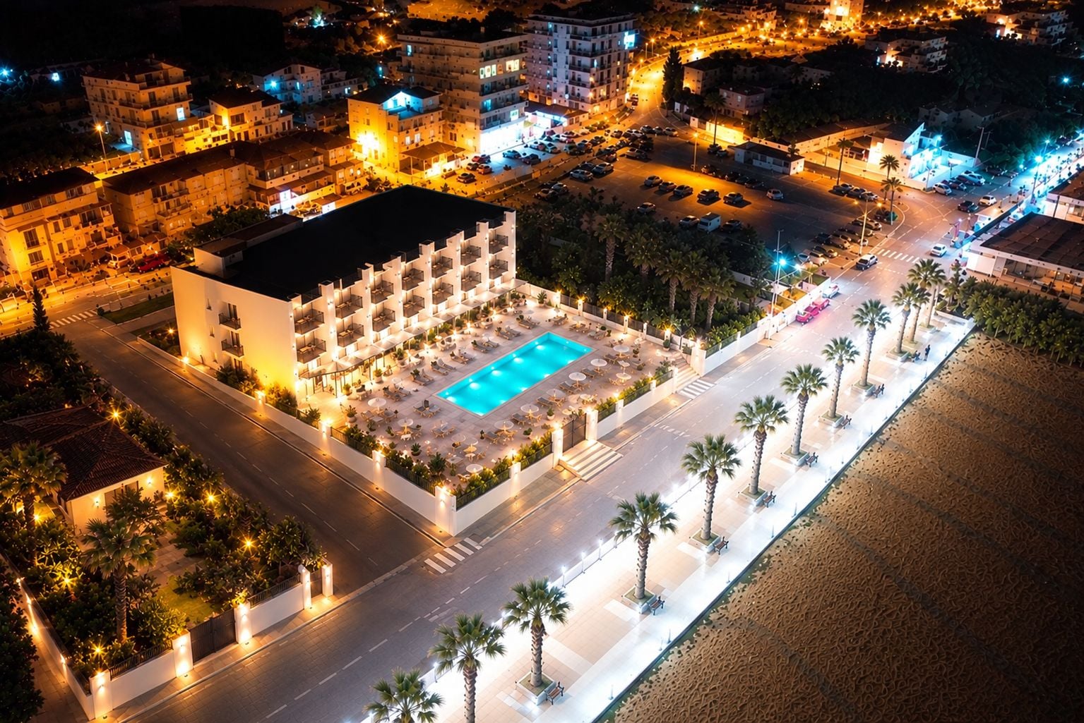 Ein Luftbild eines Hotels mit Schwimmbad, umgeben von Palmen und einer gut beleuchteten Straße.