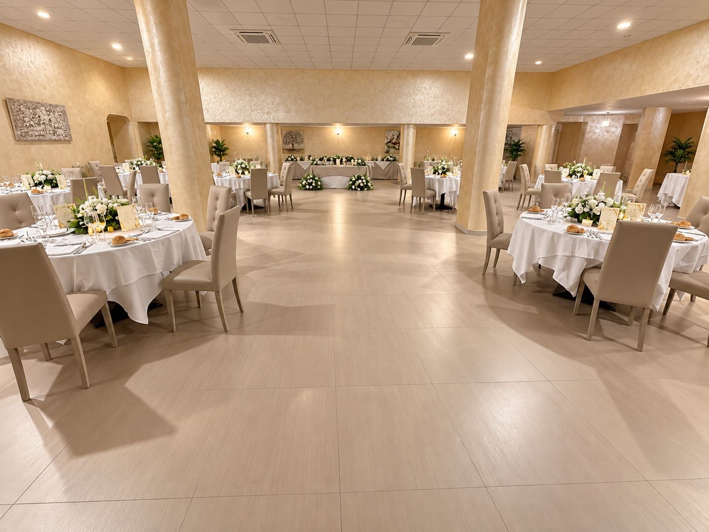 Un salón de banquetes con mesas redondas, sillas y centros de mesa florales.