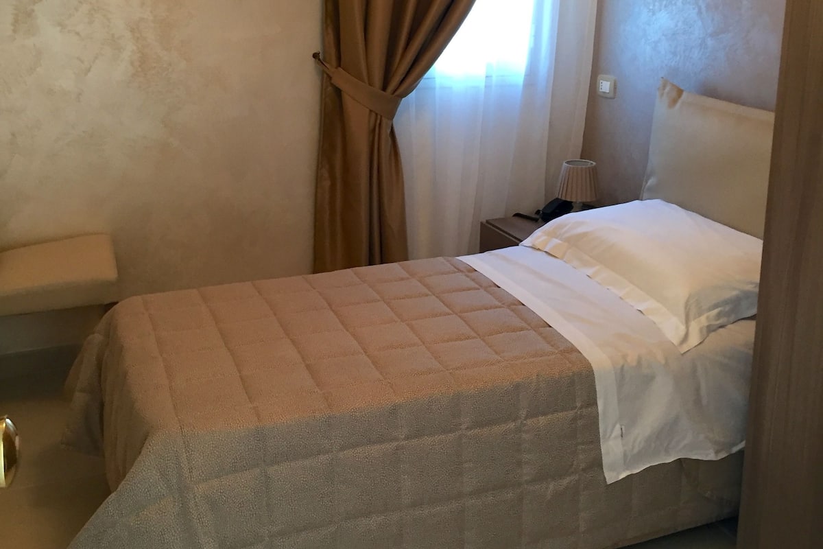 A bedroom with a bed, a nightstand, a lamp, and a window with curtains.