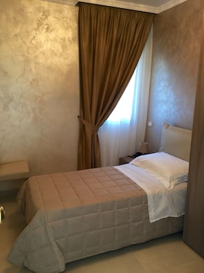 A bedroom with a bed, a nightstand, a lamp, and a window with curtains. - Hotel Riviera Palace (Porto Empedocle)