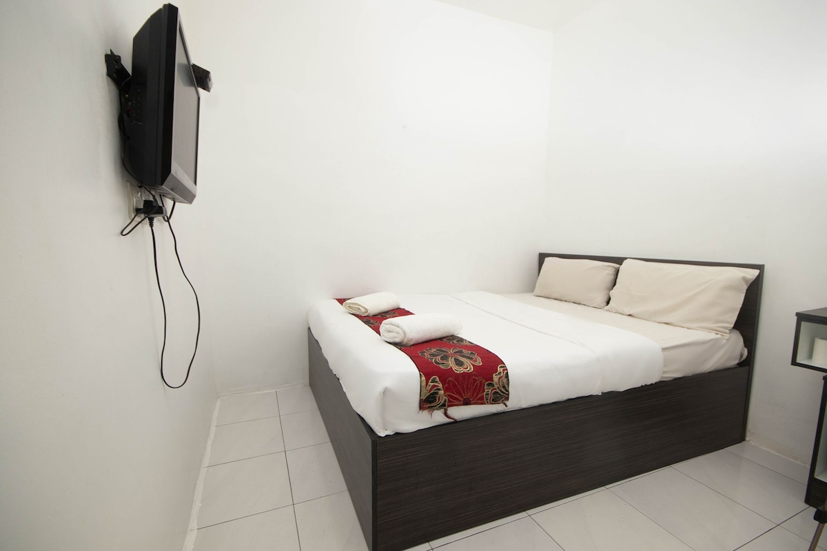 A single bed with a dark headboard, white bedding, and a red decorative throw.