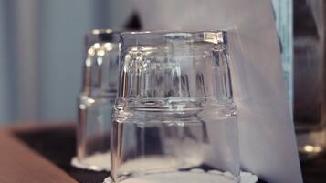 Two clear glasses on a table with a white napkin and a bottle in the background.