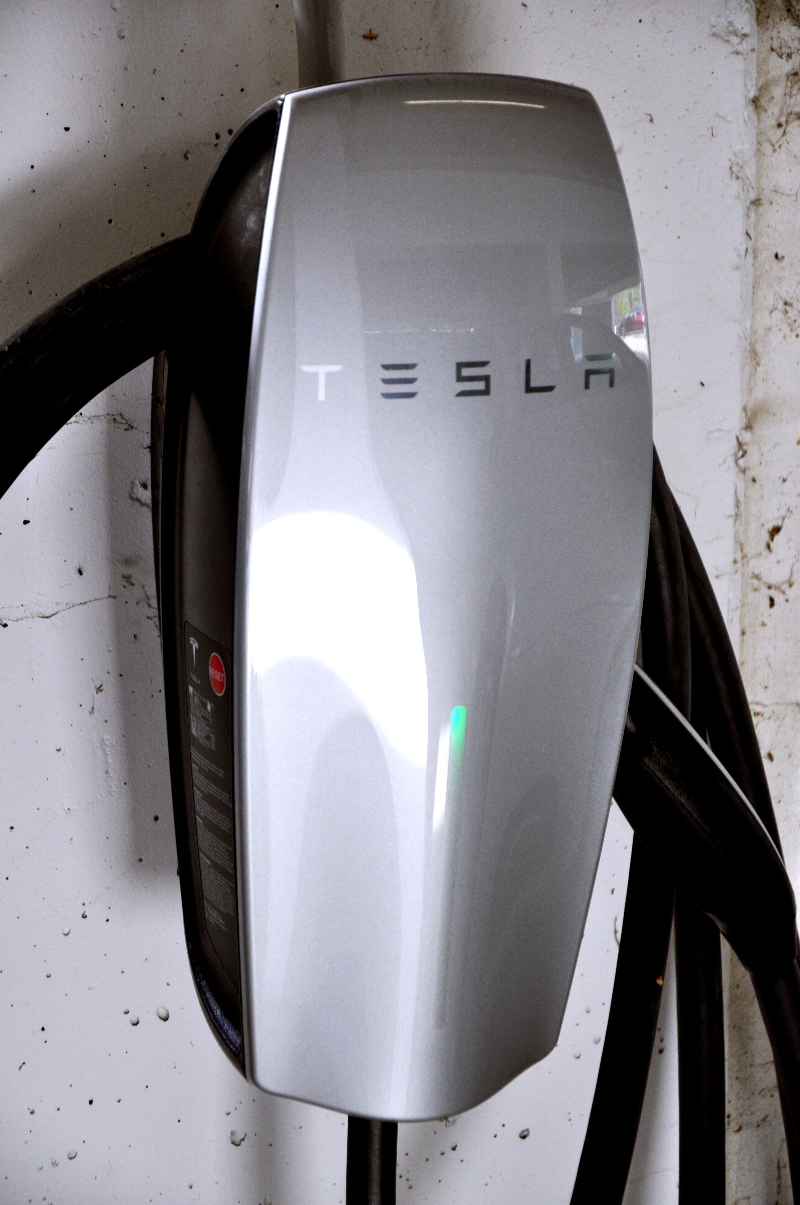 Uma estação de carregamento Tesla com acabamento metálico e o logotipo Tesla.