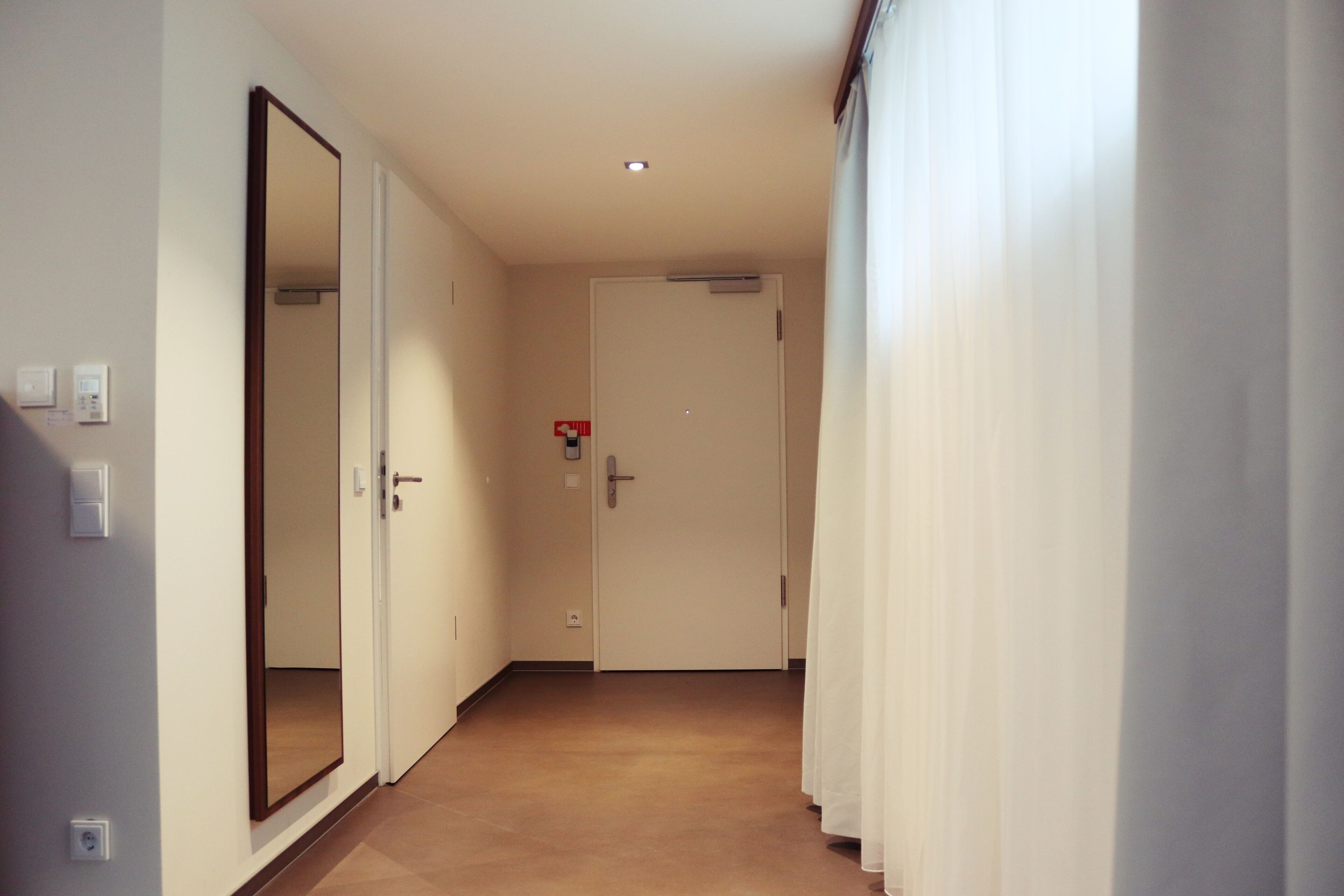 A hallway with a door, a mirror, and a light switch.