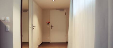 A hallway with a door, a mirror, and a light switch.